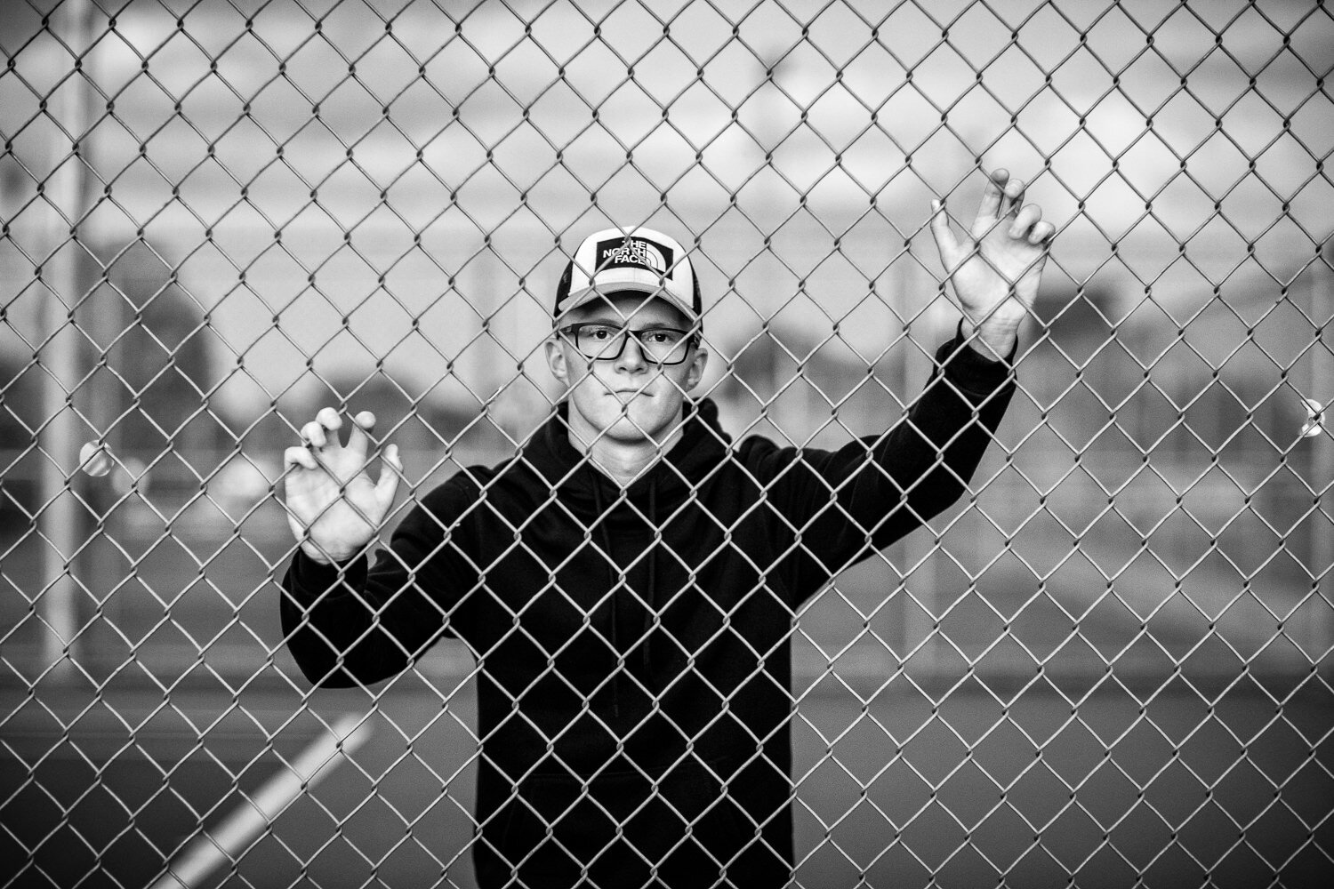 Black and white of senior at chain link fence