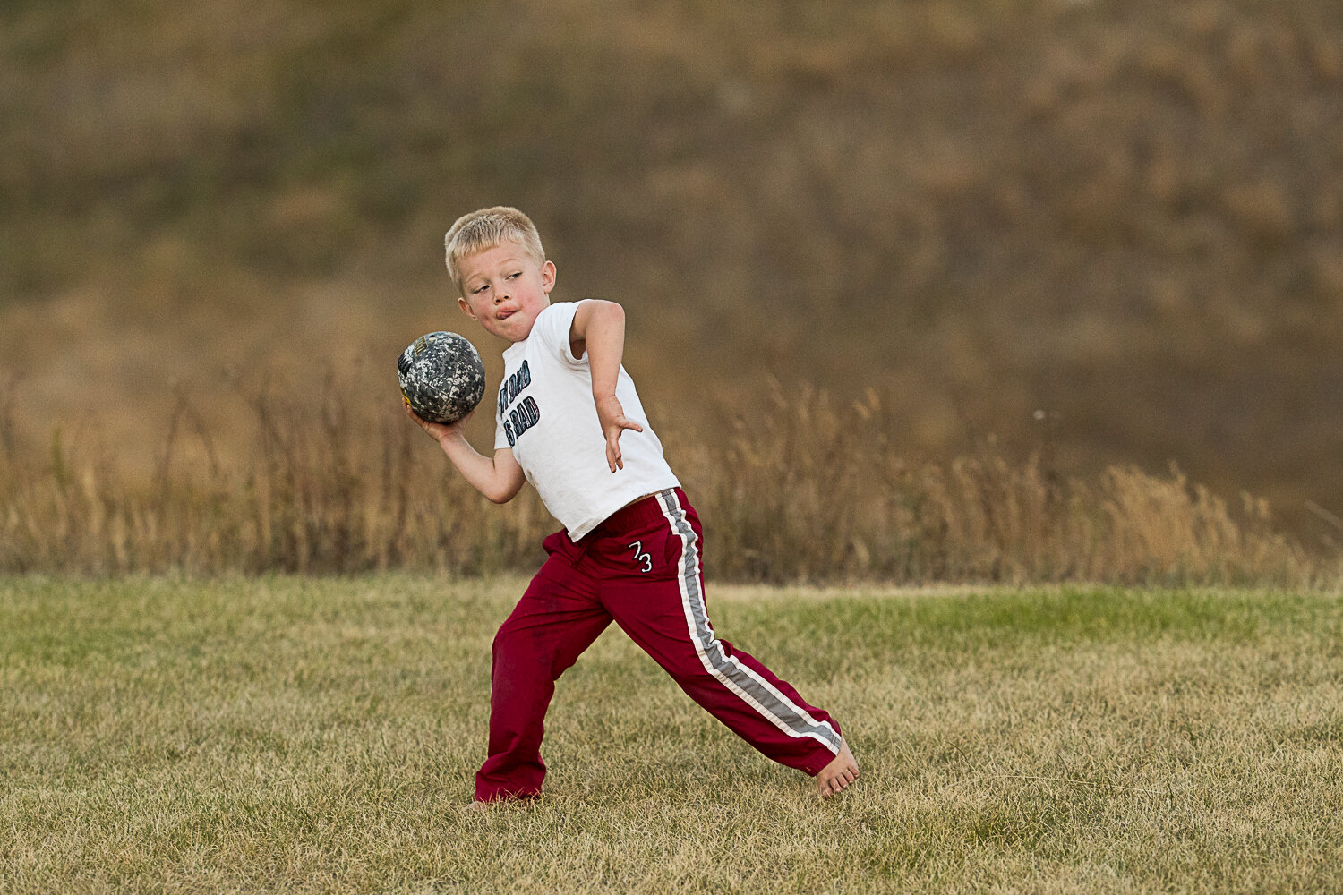 boy throwing football outside in red pants - Williston portrait photographer