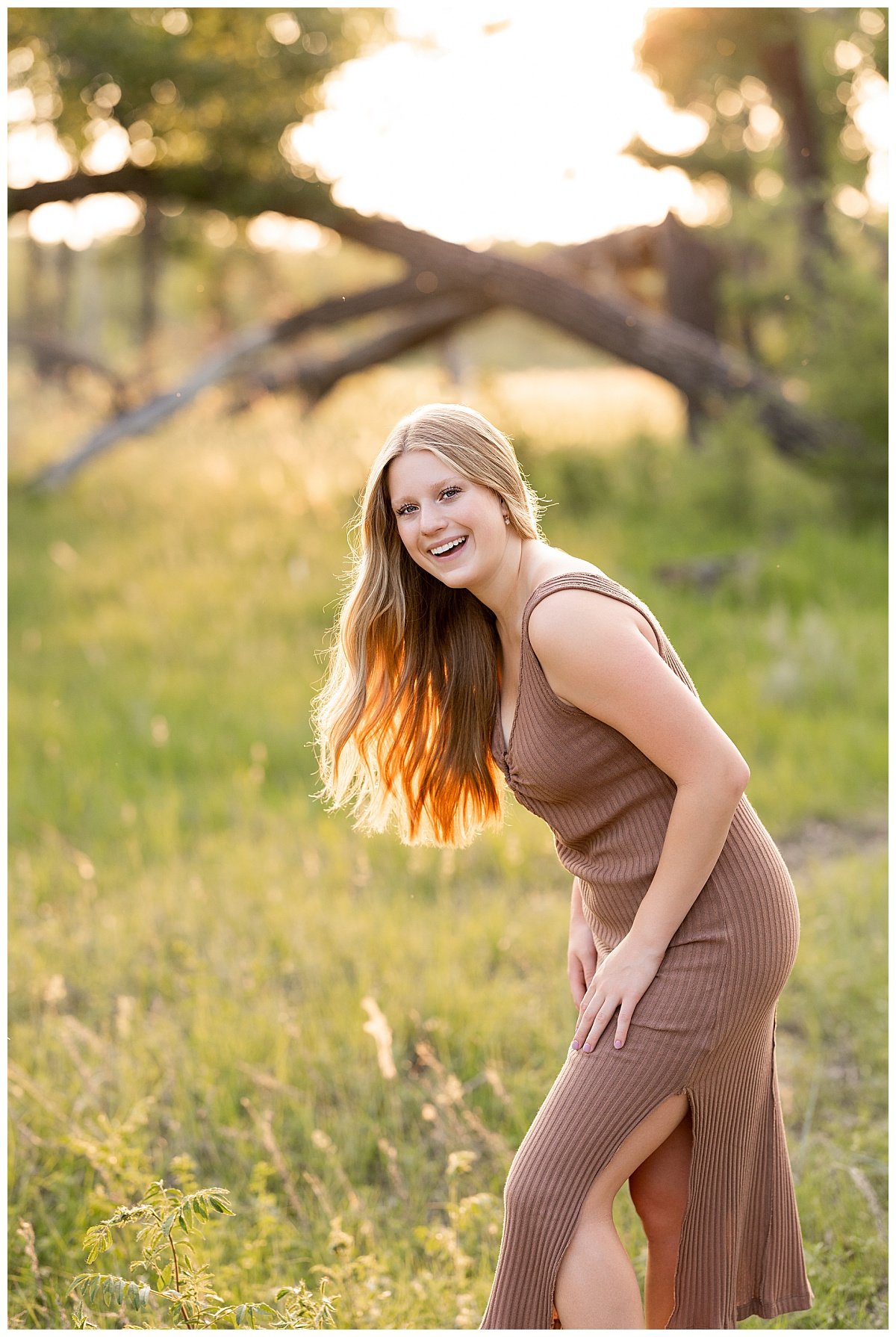 A young woman wearing a brown, knit dress smiles in the golden hour sunlight in North Dakota during an outdoor session with Kellie Rochelle Photography.