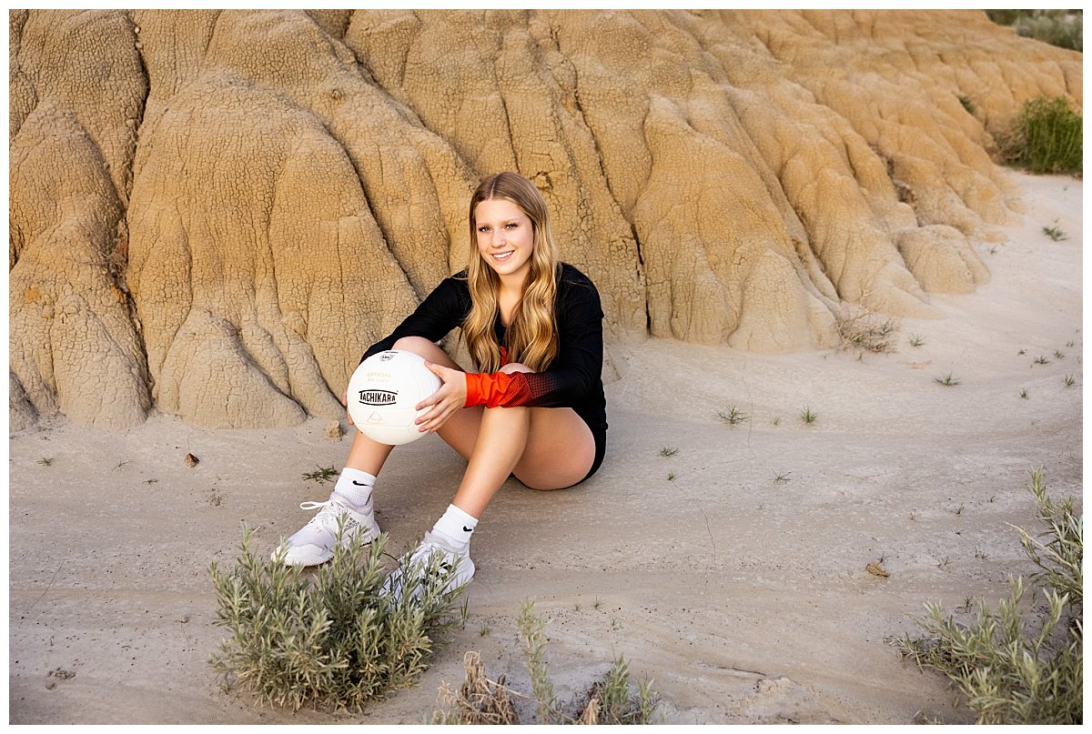 A senior volleyball player wears her uniform and poses with the ball in the North Unit at Theodore National Park.