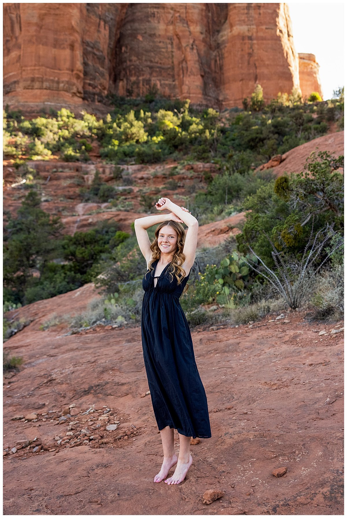 A North Dakota high school senior poses her arms over her head on a red rock formation in Sedona, AZ while wearing a black maxi dress.