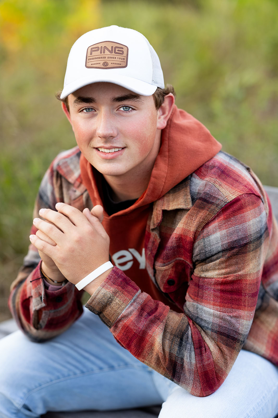 Senior boy wearing flannel and white baseball cap sitting on a bench.