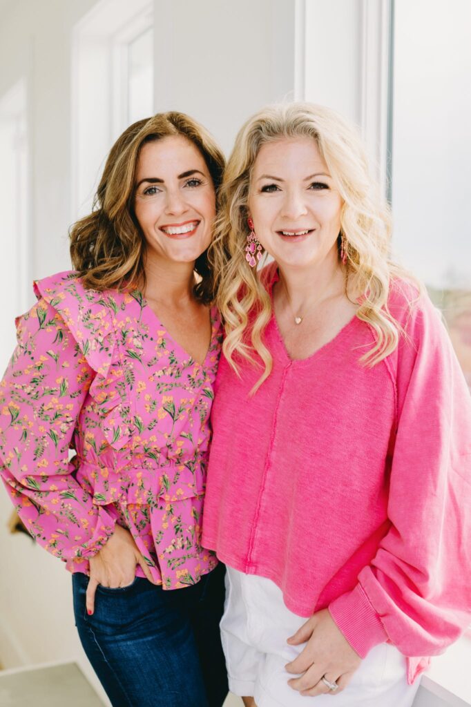 Texas based photographer and educator, Sabrina Gebhardt, is pictured with Kellie Llewellyn of Kellie Rochelle Photography, both wearing pink blouses, during a photoshoot in Destin, FL.