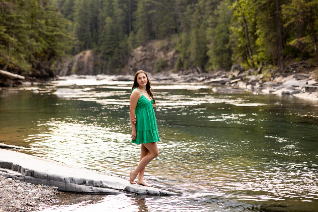 A young woman with long, brunette hair is photographed wearing a green dress during a senior photoshoot at Glacier National Park with senior photographer, Kellie Rochelle Photography. 