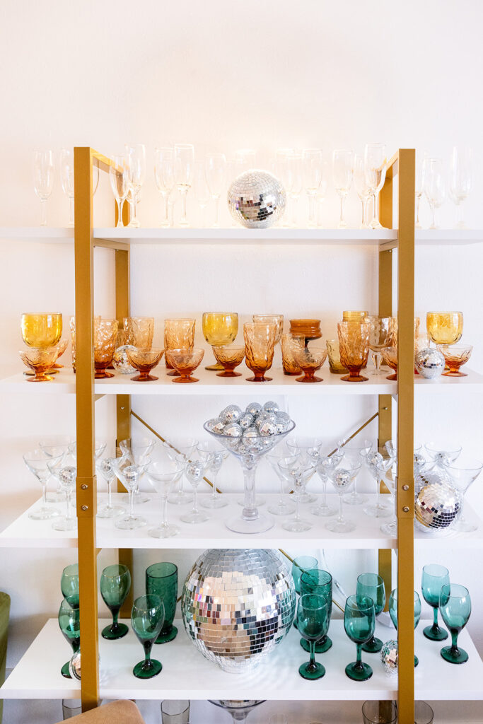 A collection of colorful glasses displayed on marble & gold shelves available for rent from House of Style, a Williston, ND based event planning business, is showcased. 