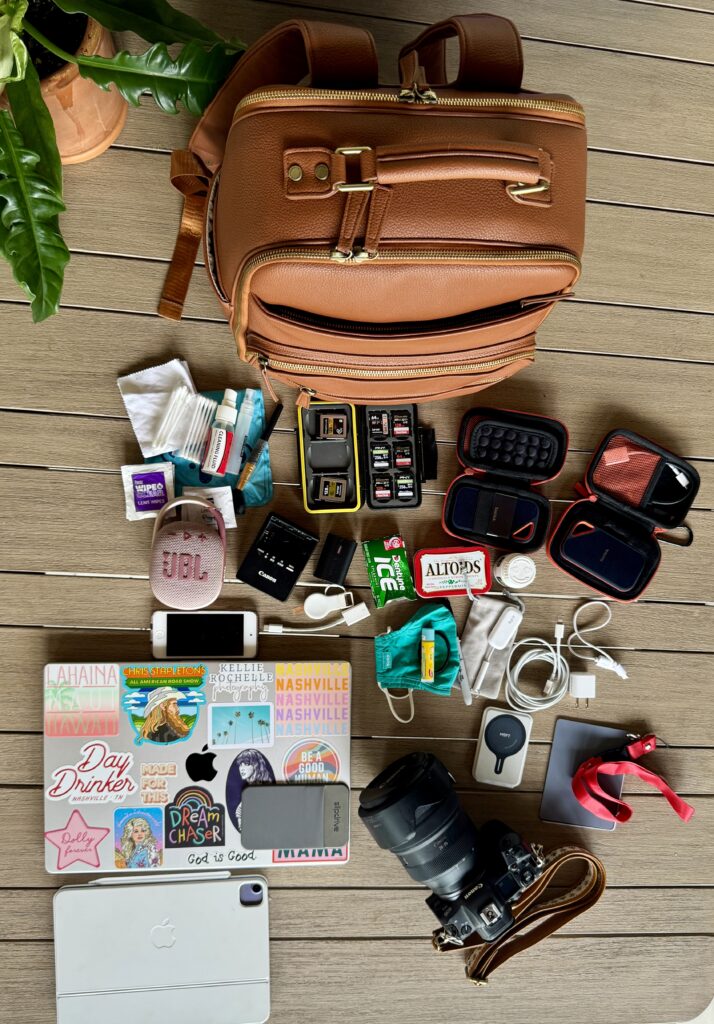 A flat lay shot displays the contents of North Dakota travel photographer and travel educator, Kellie Llewellyn of Kellie Rochelle Photography, camera bag including photography gear, portable speakers, her macbook, and several other odds & ends she brings along to all travel sessions.