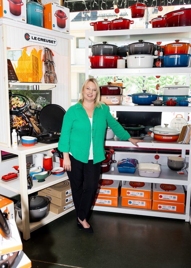 Cooks on Main owner, Angela, stands before the selection of high end dutch ovens available for purchase in her Williston storefront during a woman owned business branding session with Kellie Rochelle Photography.