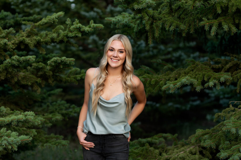 A Williston, ND high school senior girl is photographed near the evergreens at Lewis & Clark State Park during a senior photoshoot with Kellie Rochelle Photography.