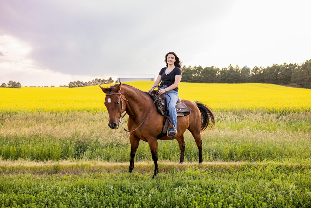 Senior girl riding her horse with canola fields in background 