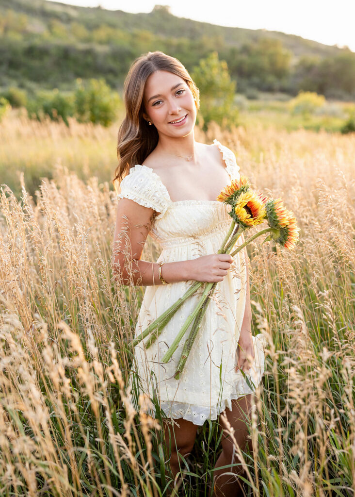 Bonny wearing a soft yellow dress, holding flowers her mom brought to her senior session