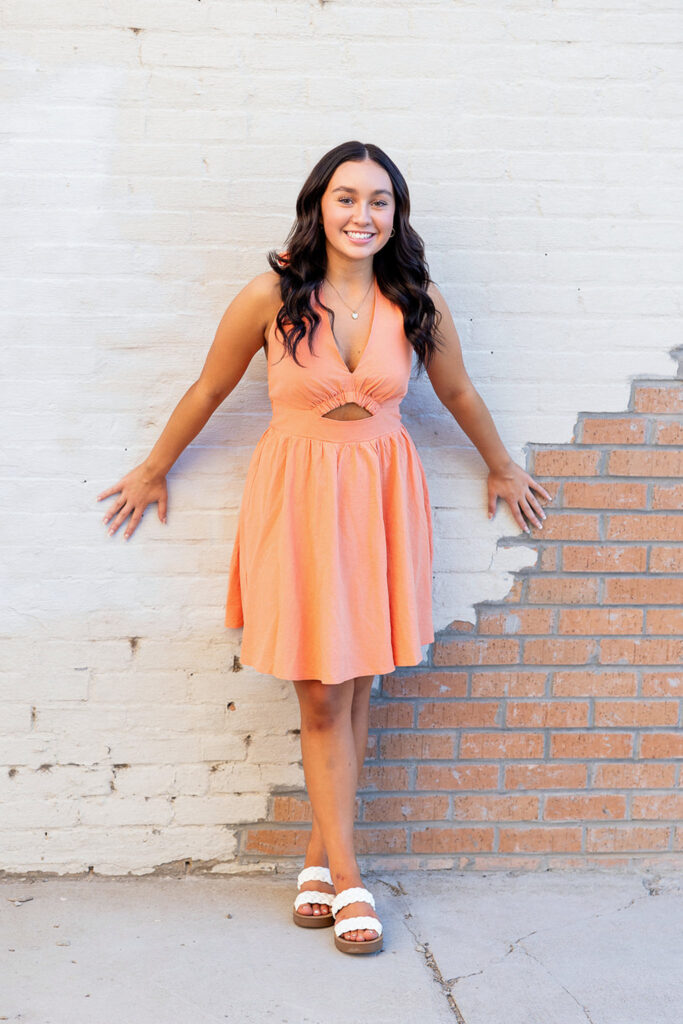 Jayla’s senior photos in an orangey-peach dress in a downtown setting, capturing urban senior portrait style.