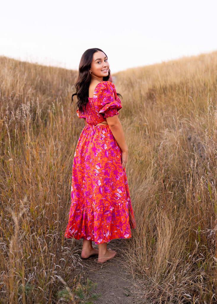 Jayla’s senior session in North Dakota, wearing a pink floral dress with side cutouts, standing in the sand.