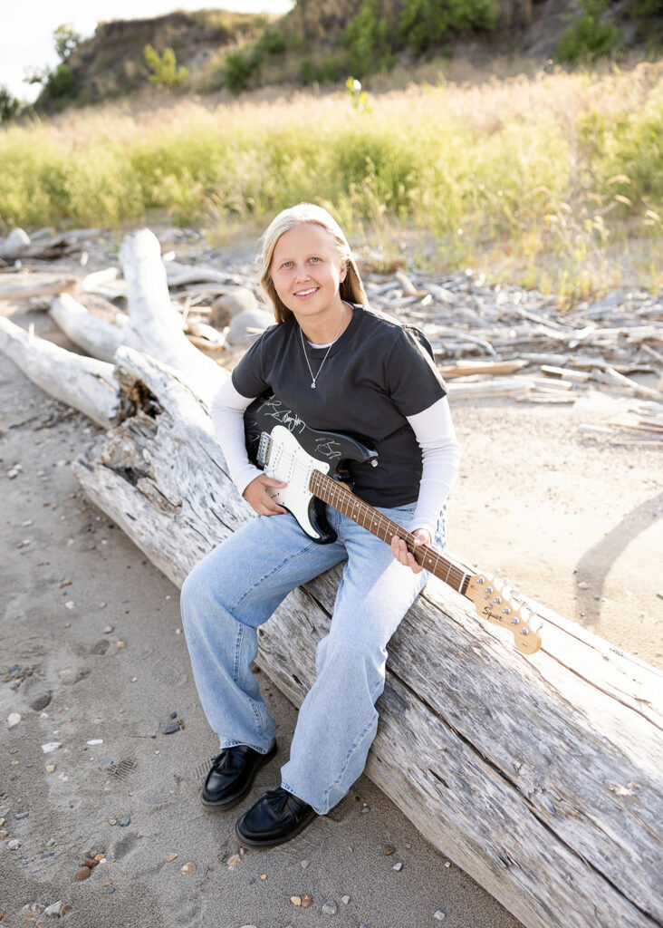 North Dakota senior photographer at Lake Sakakawea – A senior posing on the driftwood by the lake with tall grass in the background.