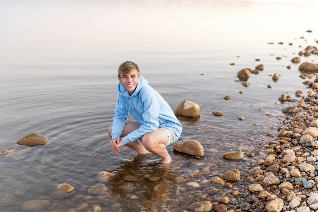 Grady standing by driftwood and sand during golden hour senior session