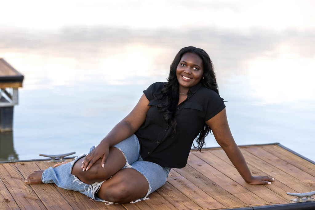 Destiny smiling on a dock in ripped jeans and black top during her senior session