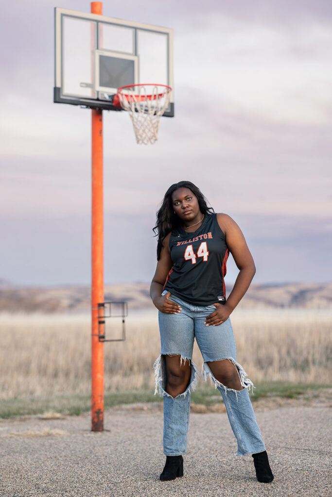 Williston senior wearing basketball jersey posing under a dramatic sunset sky
