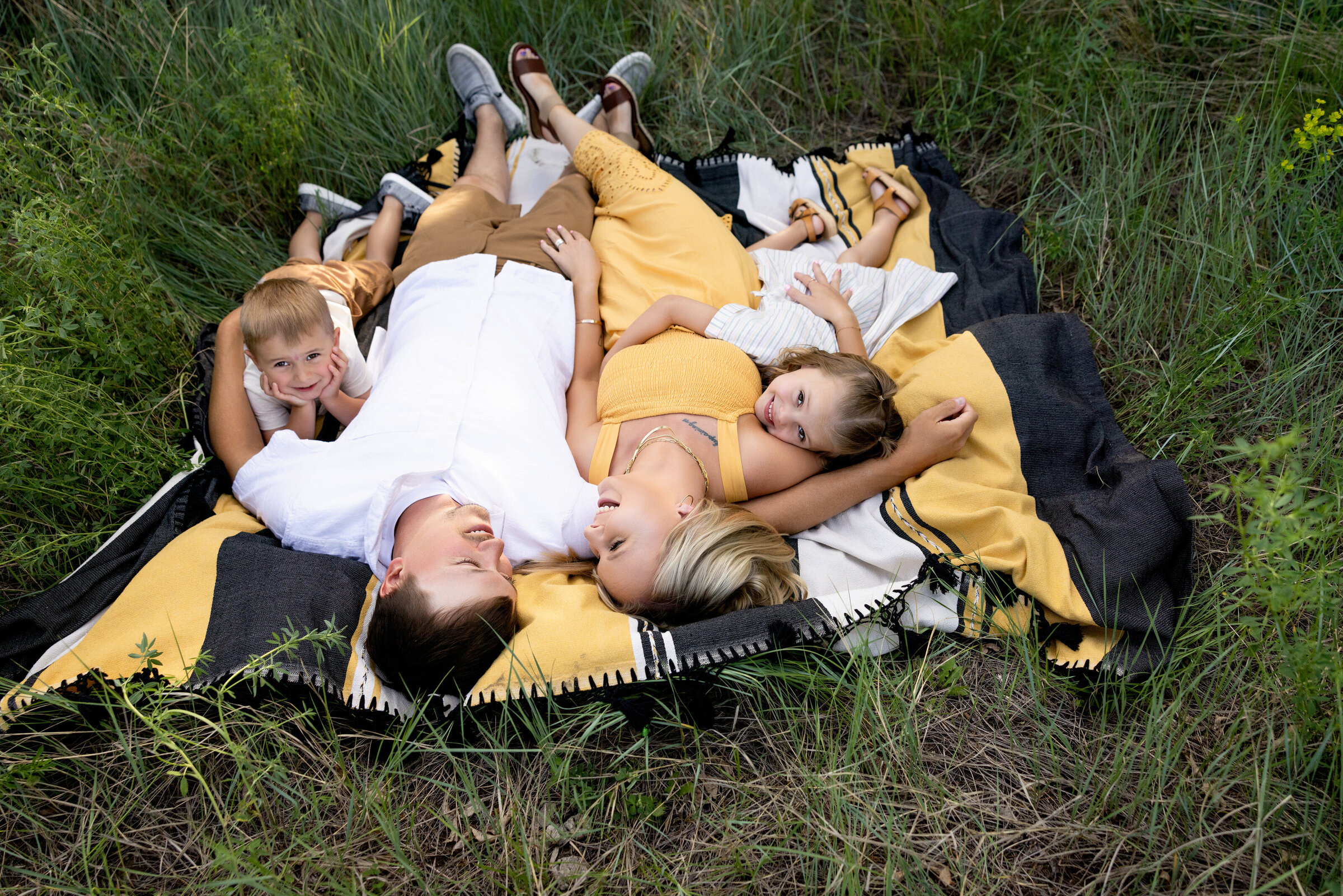 A joyful family snuggles on a blanket in tall grass—an ideal moment for photography tips for beginners.







