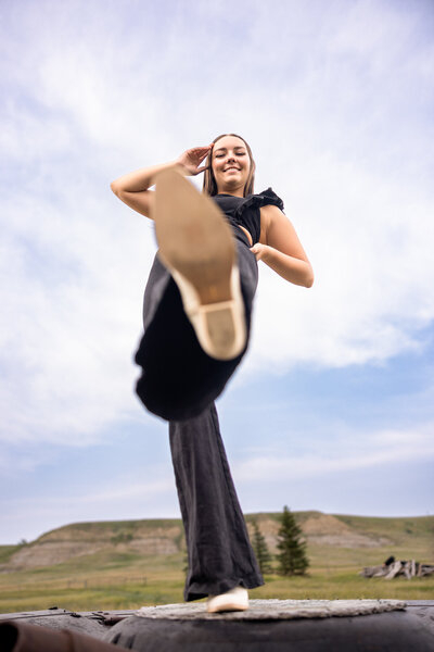 Confident senior Sunday girl kicks toward camera, sky wide behind her.