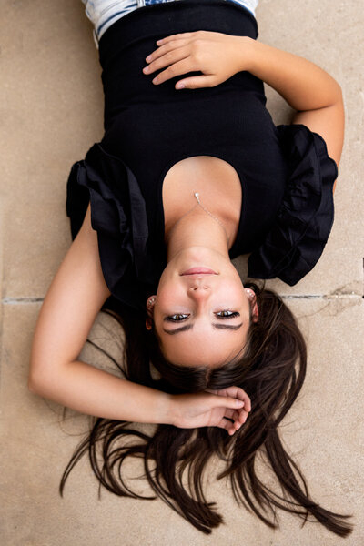 Senior girl lies on stone floor, confidently gazing up.