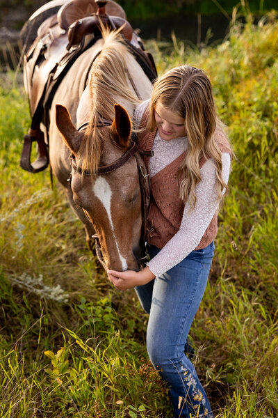 Senior girl gently feeds horse in golden field, sharing quiet moment.