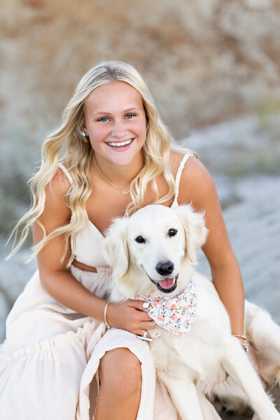 Blonde senior girl beams beside fluffy pup, both glowing with joy.