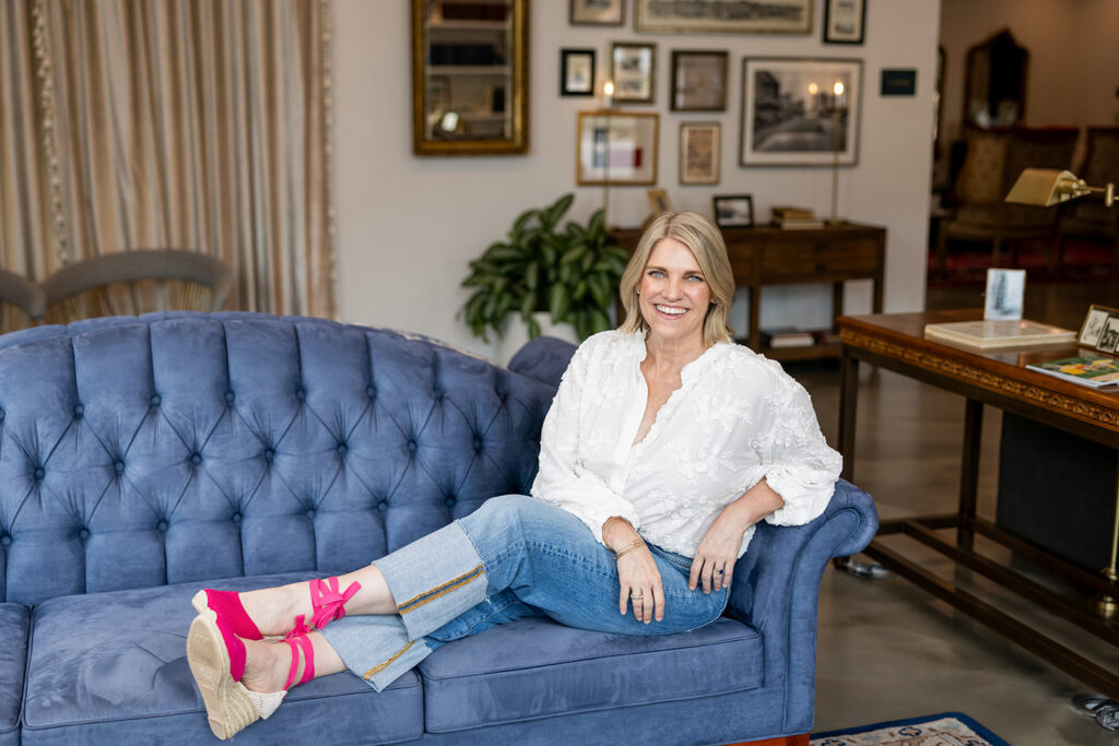 A woman wearing a white blouse & cuffed jeans relaxes on a blue velvet couch during a visit to Austin Texas