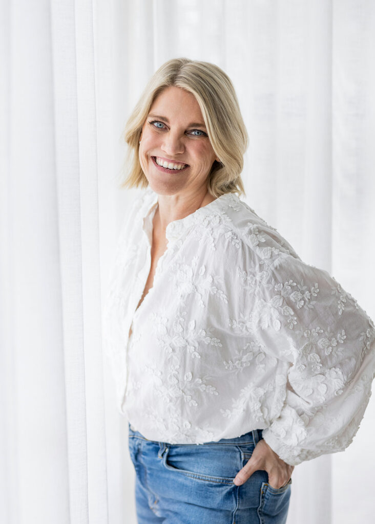 A blonde woman smiles for a headshot before a white backdrop during an Austin TX branding session