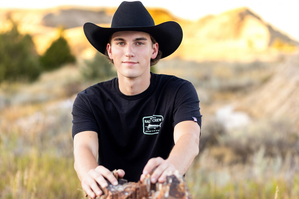 Hudson wearing cowboy hat holding his gun, framed by tall grass