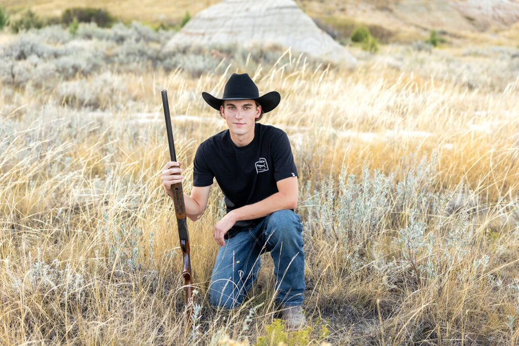 Hudson wearing cowboy hat holding his gun, framed by tall grass