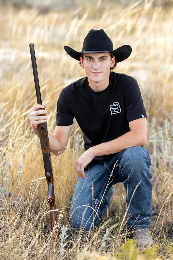 Hudson wearing cowboy hat holding his gun, framed by tall grass