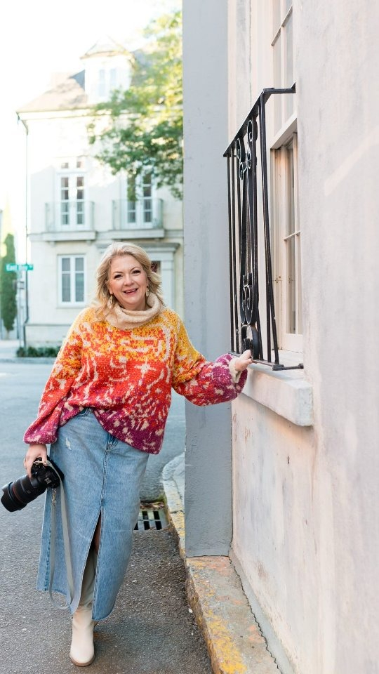 a photographer leaning against a wall holding her camera