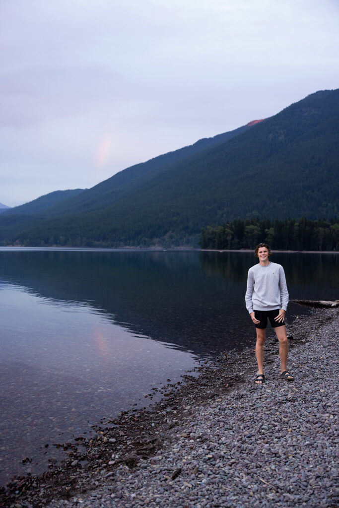 A senior boy is photographed next to the water at lake mcdonald trail glacier national park