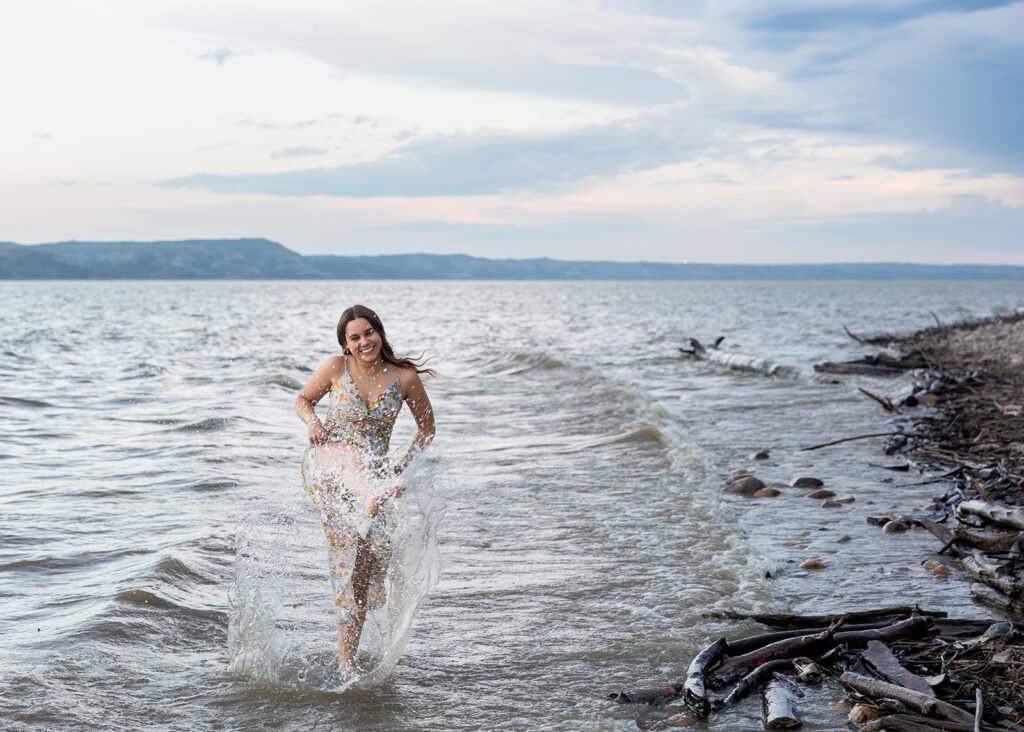 A young woman in a floral dress splashes in the water for North Dakota senior photos 