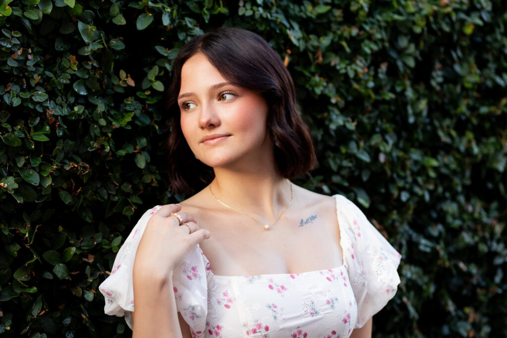 Senior girl in floral dress posing by greenery
