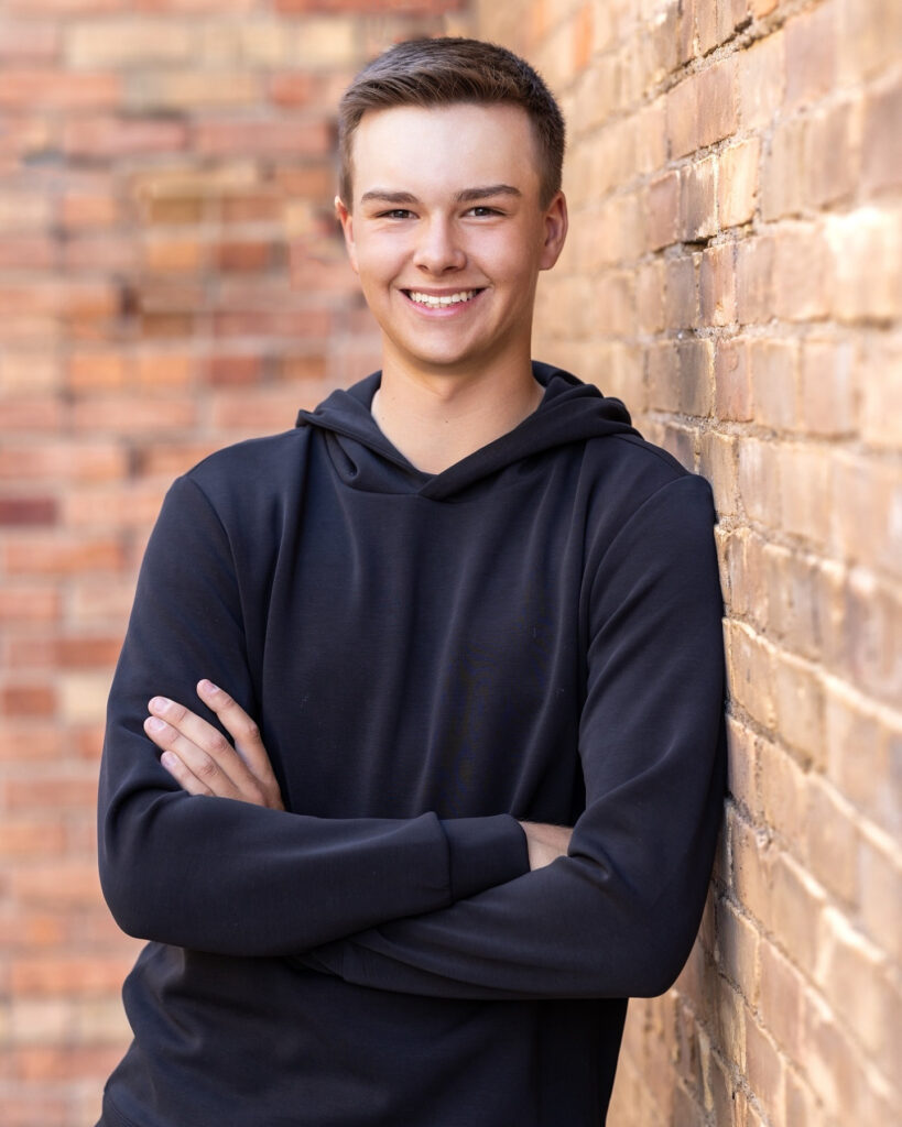 Smiling senior boy in a black hoodie leaning against a brick wall, representing confidence and clarity after creative burnout.