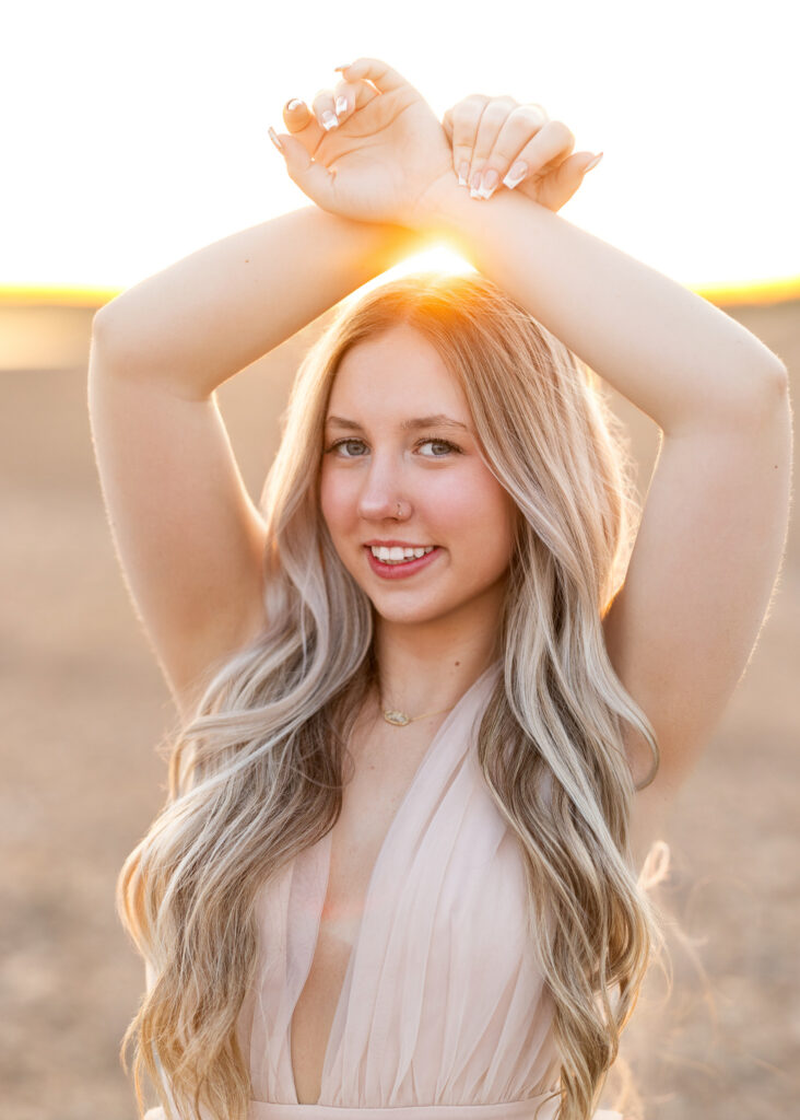 Hailey in champagne ruffle mini dress on lake rocks at sunset