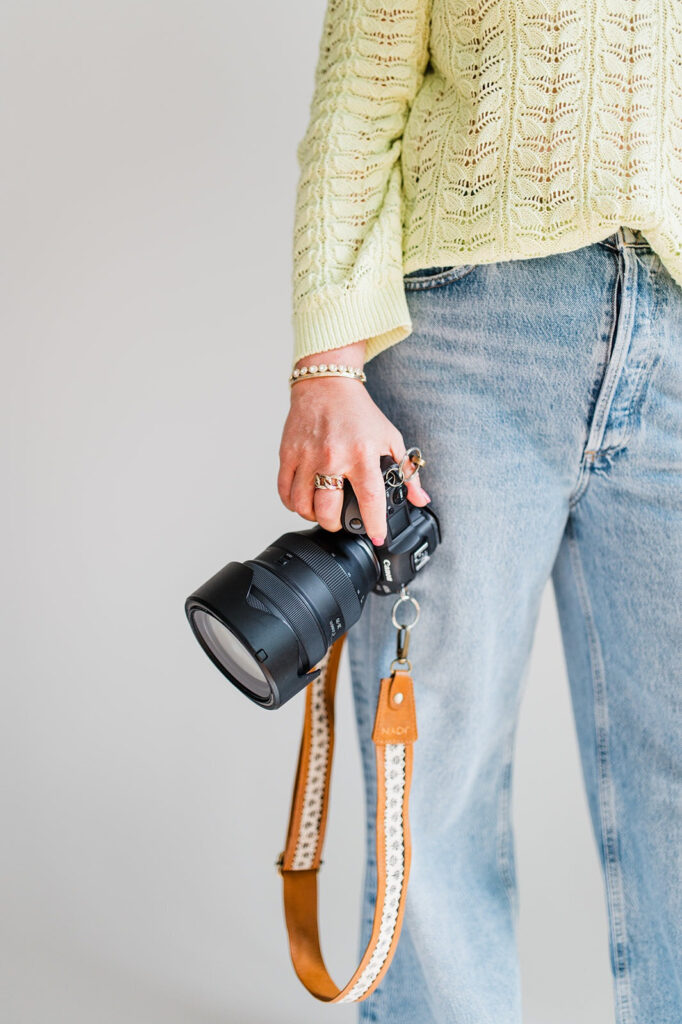 Close-up of a person wearing a yellow sweater and jeans, holding a professional camera by their side.