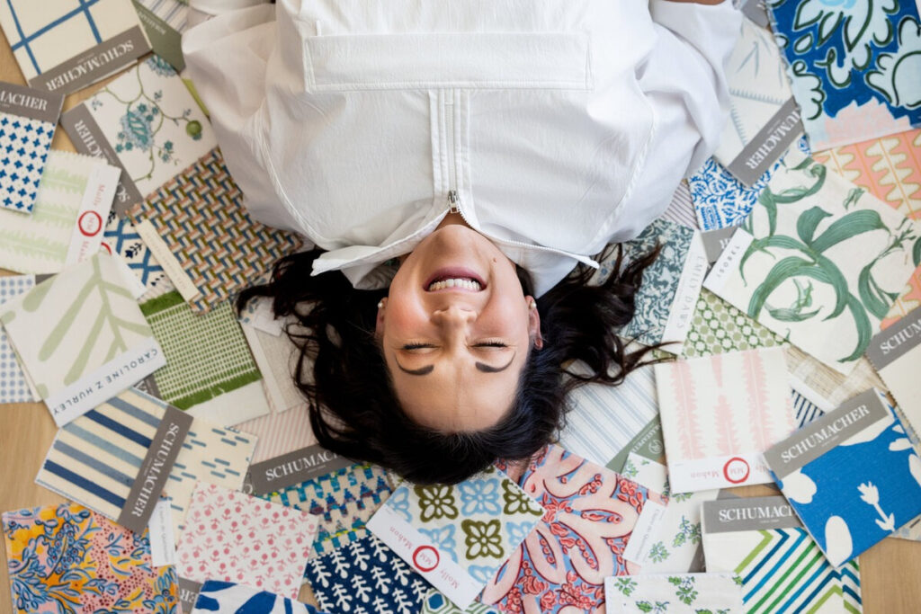Smiling woman lying on floor surrounded by colorful fabric samples, brainstorming creative business growth strategies.