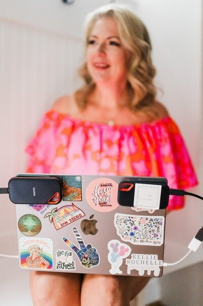 Photographer working on laptop covered in stickers, planning business growth strategies in a bright workspace.
