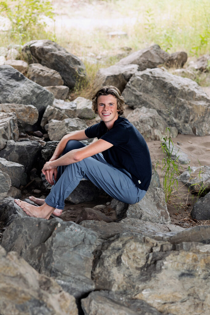 A high school senior boy is seated on the rocks at Glacier National Park during a destination photoshoot in Montana