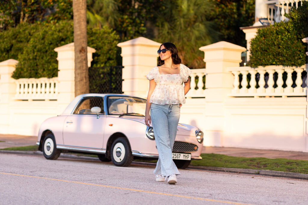 A high school senior girl wears sunnies as she struts away from the Pink Figgy during her travel photoshoot in Charleston SC