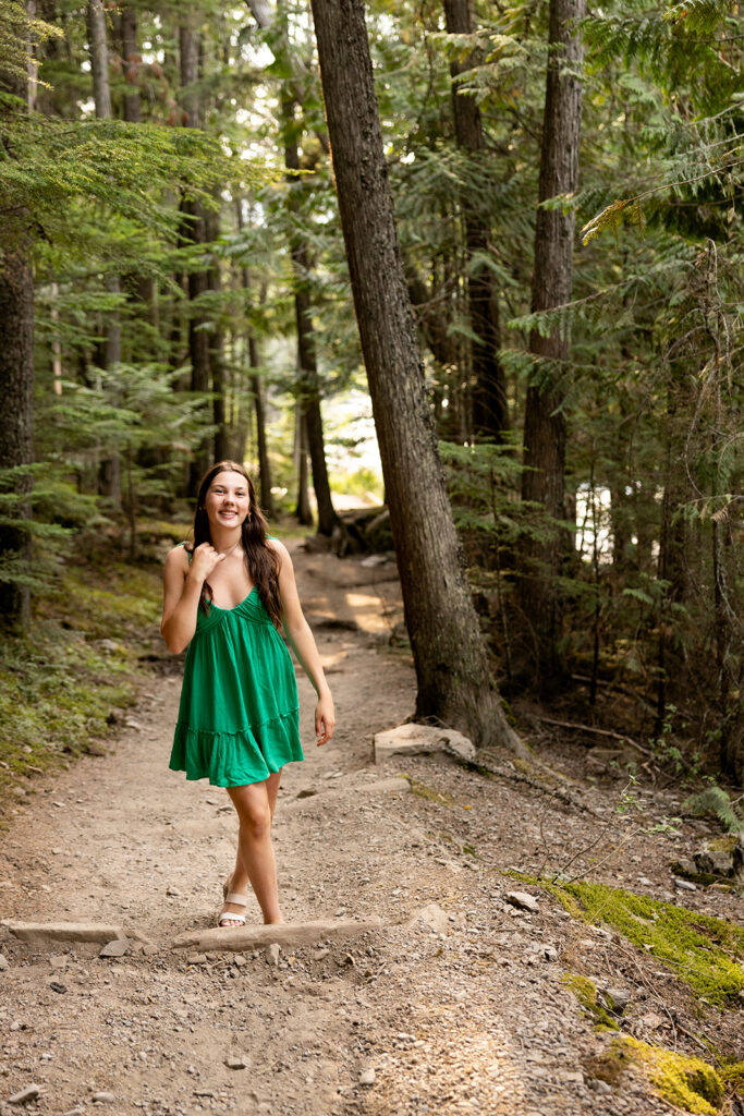 A girl in a green dress walks down a gravel path at Glacier National Park during a travel photoshoot for her senior photos
