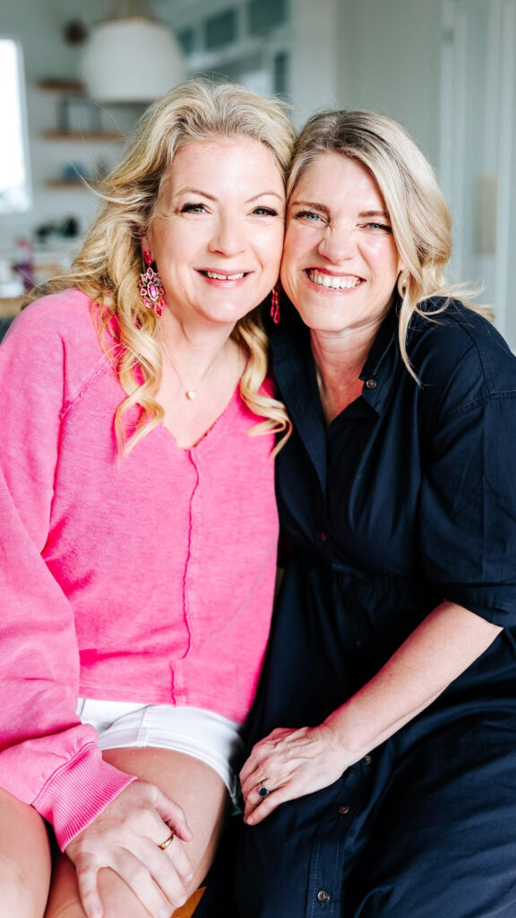Two smiling women sitting close together, sharing a warm moment and genuine connection indoors.