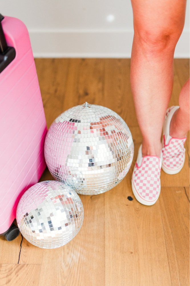 Disco balls, pink suitcase, and checkered shoes capture playful prep for a travel session in the fall.