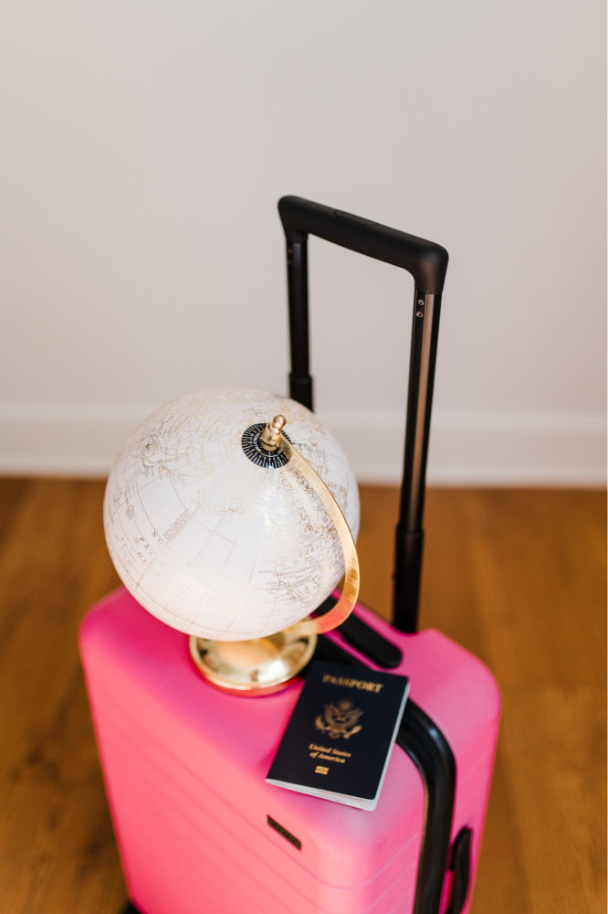 Pink suitcase with globe and U.S. passport, perfect for planning a travel session in the fall.