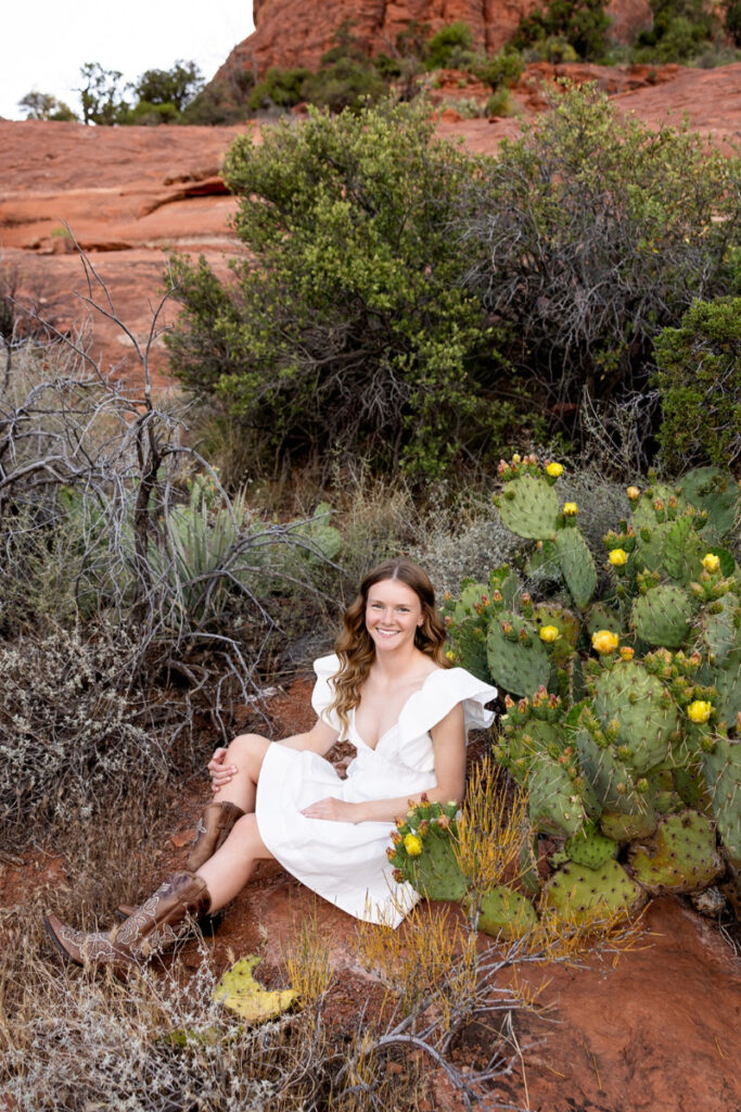 Smiling senior girl in white dress among cacti during off-season travel sessions in desert terrain.
