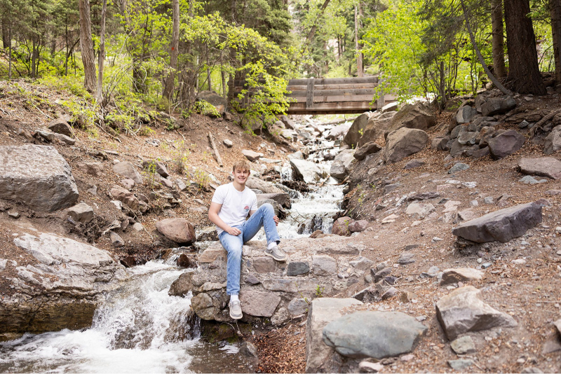 Senior guy sitting on creek rocks during off-season travel sessions in a forested mountain location.