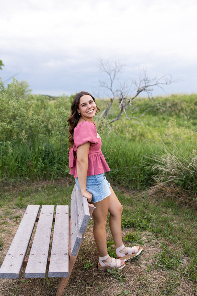 Senior portrait leaning against bench wearing mauve top