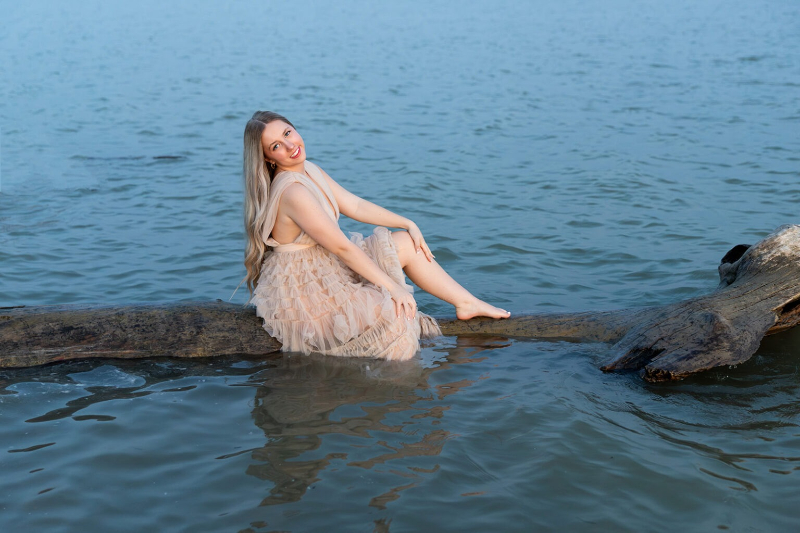 Woman in soft tulle dress sitting on driftwood in lake for a travel session guide for clients.