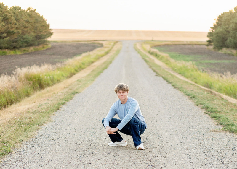 Senior boy squatting on a rural road at sunset, ideal for a travel session guide for clients.